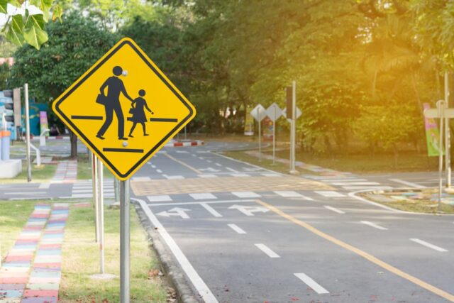 Yellow pedestrian crossing sign on a sunny road, symbolizing safety measures and legal protection guidance.