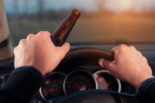 Driving under alcohol influence. Drunk driver with beer bottle in car.