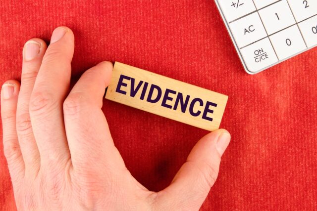 The conceptual phrase EVIDENCE made up of blocks with the help of a hand on a red background