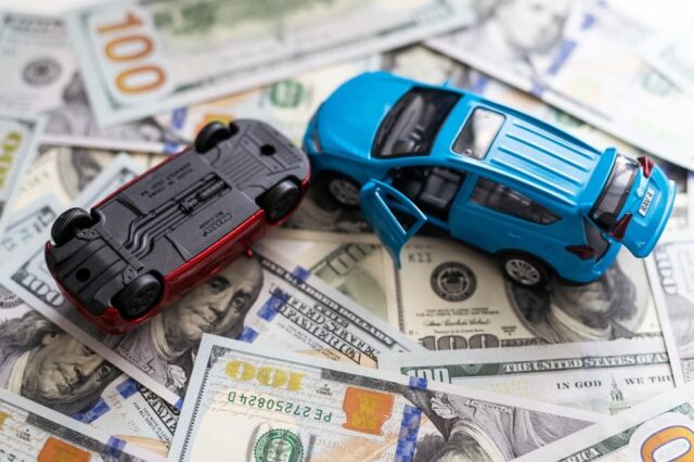 concept of car accident loss and damage. two model cars on the heap of us hundred dollars. 